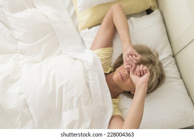 High Angle View Of Mature Woman Rubbing Eyes While Lying In Bed At Home