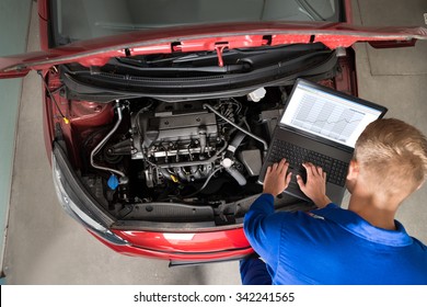 High Angle View Of Mechanic Examining Car Engine With Help Of Laptop