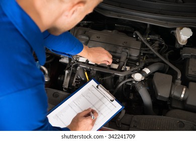 High Angle View Of A Mechanic Standing Near Car Writing On Clipboard In Garage