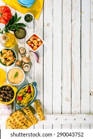 High Angle View Of Mediterranean Appetizers Spread Out On Rustic White Wooden Picnic Table With Copy Space