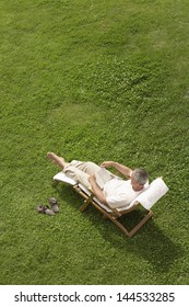 High Angle View Of Middle Aged Man Reading Book On Deck Chair In Garden