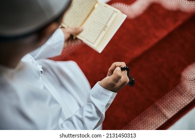 High angle view of Middle Eastern man holding misbaha beads while reading Koran during a prayer at home. 