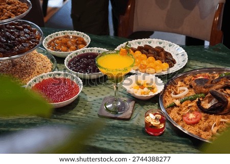 High angle view of Middle Eastern feast with Mandi rice, grilled chicken, dates, and fresh fruit juice on a green tablecloth.