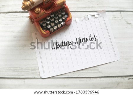 High angle view of miniature typewriter and paper written with Meeting Minutes on white wooden background.