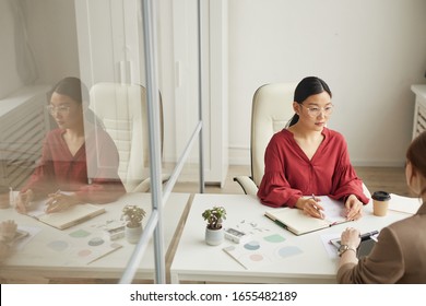 High Angle View At Modern Asian Businesswoman Talking To Client While Working At Desk In White Office Cubicle, Copy Space