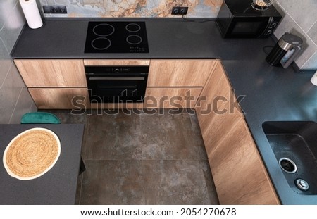 High angle view of a modern compact fitted kitchen with wooden cabinets, stone countertops and built in stove and hob with small appliances on the work surface