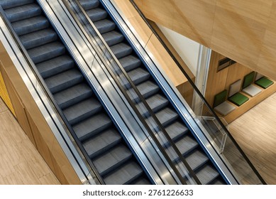 High angle view of modern parallel escalators in a building interior with wooden walls. Architecture, urban transportation and business concept.