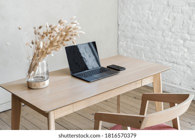 High Angle View Of Modern Smartphone Near Laptop Computer With Blank Screen Display On Wooden Office Table, Dry Plants In Vase And Comfort Chair. Contemporary Apartment With Workplace In Living Room