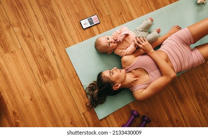 High angle view of a mom lying on an exercise mat with her baby. Mother and baby taking a break from working out. New mom bonding with her baby during her post-natal fitness routine. - Shutterstock ID 2133430009