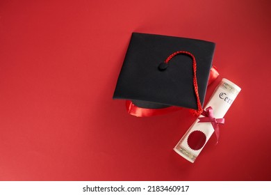 High Angle View Of Mortar Board And Scroll Of Certificate Against Red Background