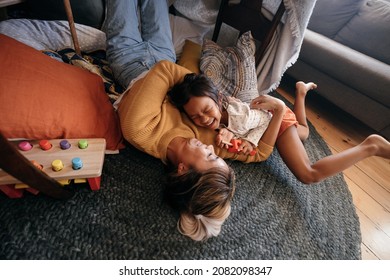 High Angle View Of A Mother And Her Daughter Laughing Happily At Home. Cheerful Mother And Daughter Lying On The Floor In Their Play Area. Mother And Daughter Spending Some Quality Time Together.