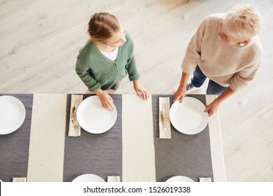 High Angle View Of Mother Setting The Table And Her Daughter Helping To Her Before The Family Dinner At Home