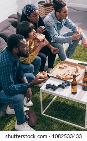 High Angle View Of Multiethnic Friends Eating Pizza And Watching American Football Match