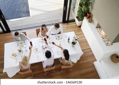 High Angle View Of Multiethnic Friends Toasting Wine Across Table At Dinner Party