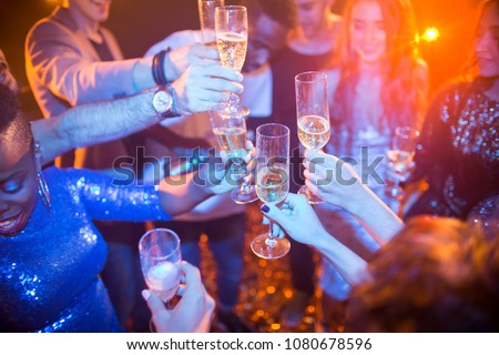 High angle view at multi-ethnic group of laughing young people enjoying dance party in nightclub and drinking champagne, focus on clinking glasses