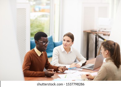High angle view at multi-ethnic team of students discussing group project sitting at desk in library, copy space - Shutterstock ID 1537798286