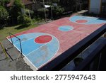 High angle view of a multipurpose outdoor sports court with red and blue painted surface for basketball and futsal. Functional public athletic facility in a school or community neighborhood area.