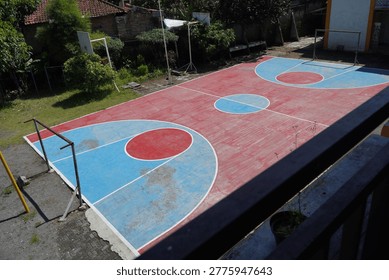 High angle view of a multipurpose outdoor sports court with red and blue painted surface for basketball and futsal. Functional public athletic facility in a school or community neighborhood area.