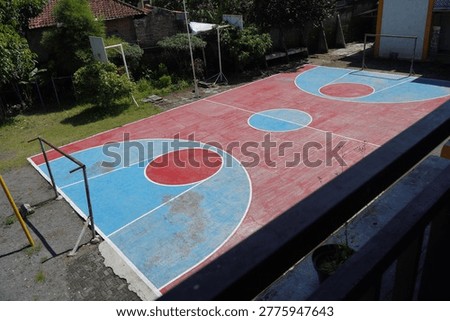 High angle view of a multipurpose outdoor sports court with red and blue painted surface for basketball and futsal. Functional public athletic facility in a school or community neighborhood area.