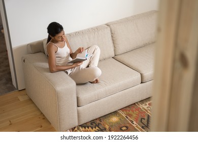 Hochwinkelaufnahme der multiethnischen Frauen, die interessantes Buch lesen, während sie die Freizeit am Wochenende allein zu Hause genießen. Buchliebhaber, Lieblingshobby, Selbstbildung, Bestsellerliteratur