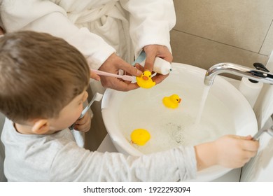 High Angle View Of The Nice Boy Playing With His Toy Ducks At The Sink While Brushing His Teeth In The Bathroom With His Family. Stock Photo