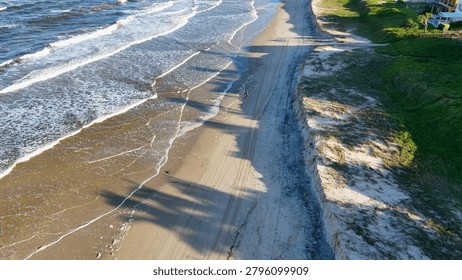 High angle view of ocean waves crashing on a sandy beach with long shadows.
