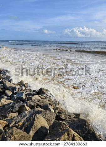 High angle view of ocean waves crashing against heavy granite boulders on a coastal sea wall under a blue sky