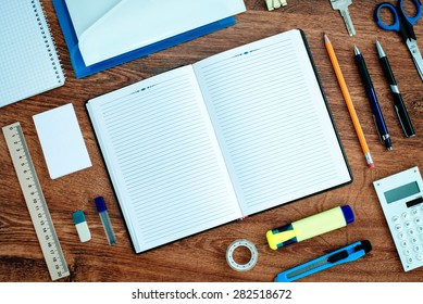 High Angle View of Office or School Supplies Neatly Organized Around Open Note Book with Blank Page on Wooden Desk Top