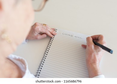 High Angle View Of Older Woman Writing LIVING WILL In Notebook (selective Focus)