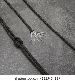 High angle view of olive drab tactical 550 paracord with knot showing exposed white inner nylon core strands on dark grey concrete textured backdrop background, utility equipment concept.