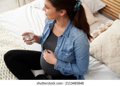 High angle view on caucasian woman in advanced pregnancy sitting on bed and drinking water
