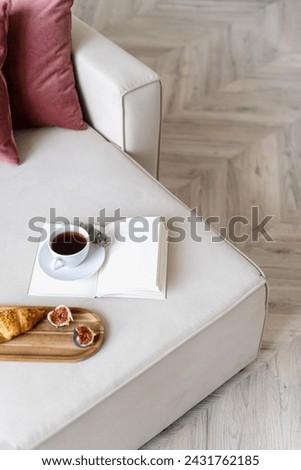 High angle view on open diary with empty page, cup of coffee and wooden tray with french croissant and fresh fig on corner of comfort couch in morning at living room. Concept of breakfast at cozy home
