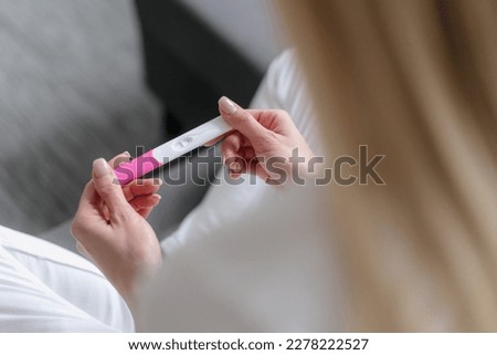 high angle view on pregnancy test in female hands, girl check and expect for result, sitting on sofa in living room, planning future