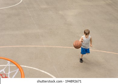 High Angle View From On Top Of The Hoop Of A Sporty Young Boy Playing Basketball On An Outdoor Court Running With The Ball