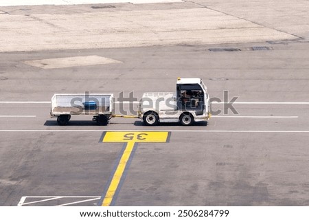 High angle view one baggage tractor-trailer (baggage tow tractor) on a service road on the tarmac of the airport with one suitcase on trolley