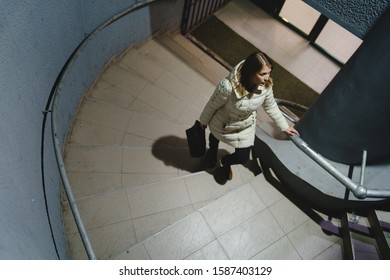 High Angle View Of One Caucasian Woman Female Girl Climbing Up The Stairs From The Building Or Metro Wearing White Jacket At Night In Winter Or Autumn Night Alone