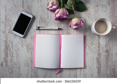 Hochwinkel-Blick auf das offene leere Notebook, Mobiltelefon, Tasse Kaffee und Rosenstrauß auf weißem Holztisch