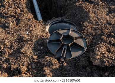 High Angle View of an Open Plastic Inspection Chamber and Underground PVC Pipe in a Soil Trench
