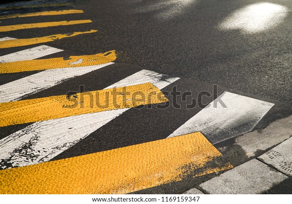 High angle view over a provisional yellow\
pedestrian crossing, painted over an older white one, in the grey\
asphalt of the road, changing the direction of the path, for a new\
one, Paris, France.