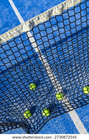 High angle view of a padel net and yellow balls on a blue artificial grass court