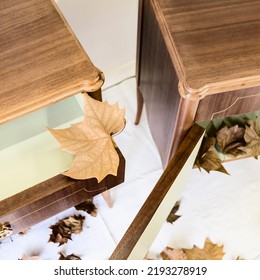 High Angle View Of A Pair Of Picturesque Wooden Small Bedtime Tables With The Door Open And A Few Dry Tree Leafs Inside It And Over The White Floor. 