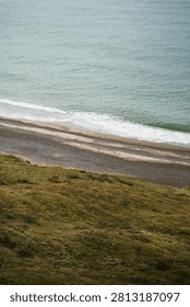 High angle view of a pebbly beach and ocean waves from a grassy cliff in Denmark
