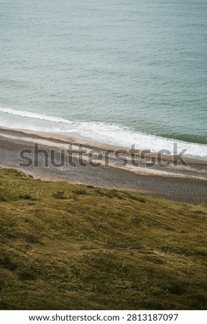 High angle view of a pebbly beach and ocean waves from a grassy cliff in Denmark