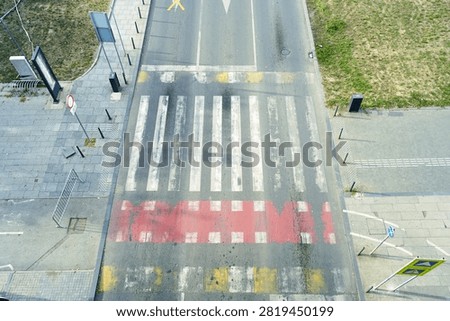 High angle view of pedestrian crossing with red bicycle lane, sidewalks, and surrounding roadway. Highlights complete street principles, multimodal corridor design, urban traffic organization, and human-centered mobility.