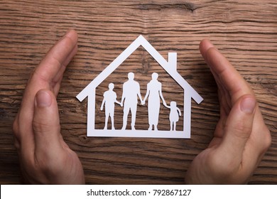 High Angle View Of Person Holding Protective Hand On Family Home On Wooden Table - Powered by Shutterstock