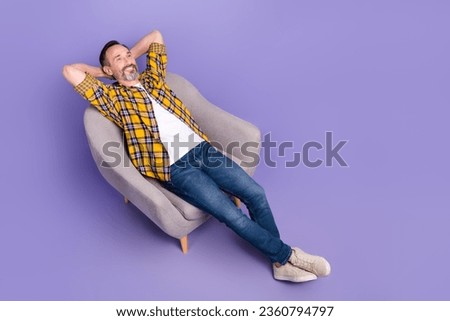 High angle view photo of cheerful man hold arms behind head lying armchair adv poster empty space isolated on purple color background