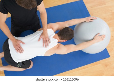 High angle view of a physical therapist assisting young man with yoga ball in the gym at hospital