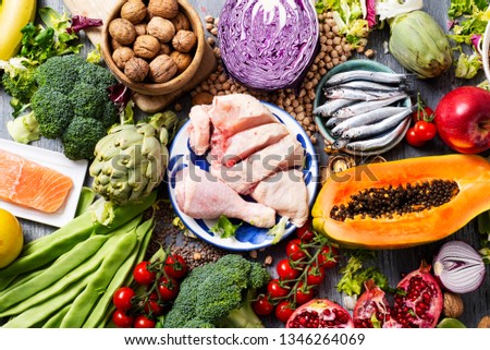 high angle view of a pile of unprocessed food, such as different raw fruits and vegetables, some legumes and nuts, some pieces of chicken and some different fishes, on a gray rustic wooden table