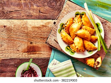 High Angle View Of Plateful Of Fresh Baked Empanada Pastries With Fresh Green Onions Served On Rustic Wooden Table With Copy Space