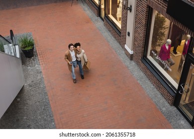 high angle view of pleased interracial couple with purchases walking in mall